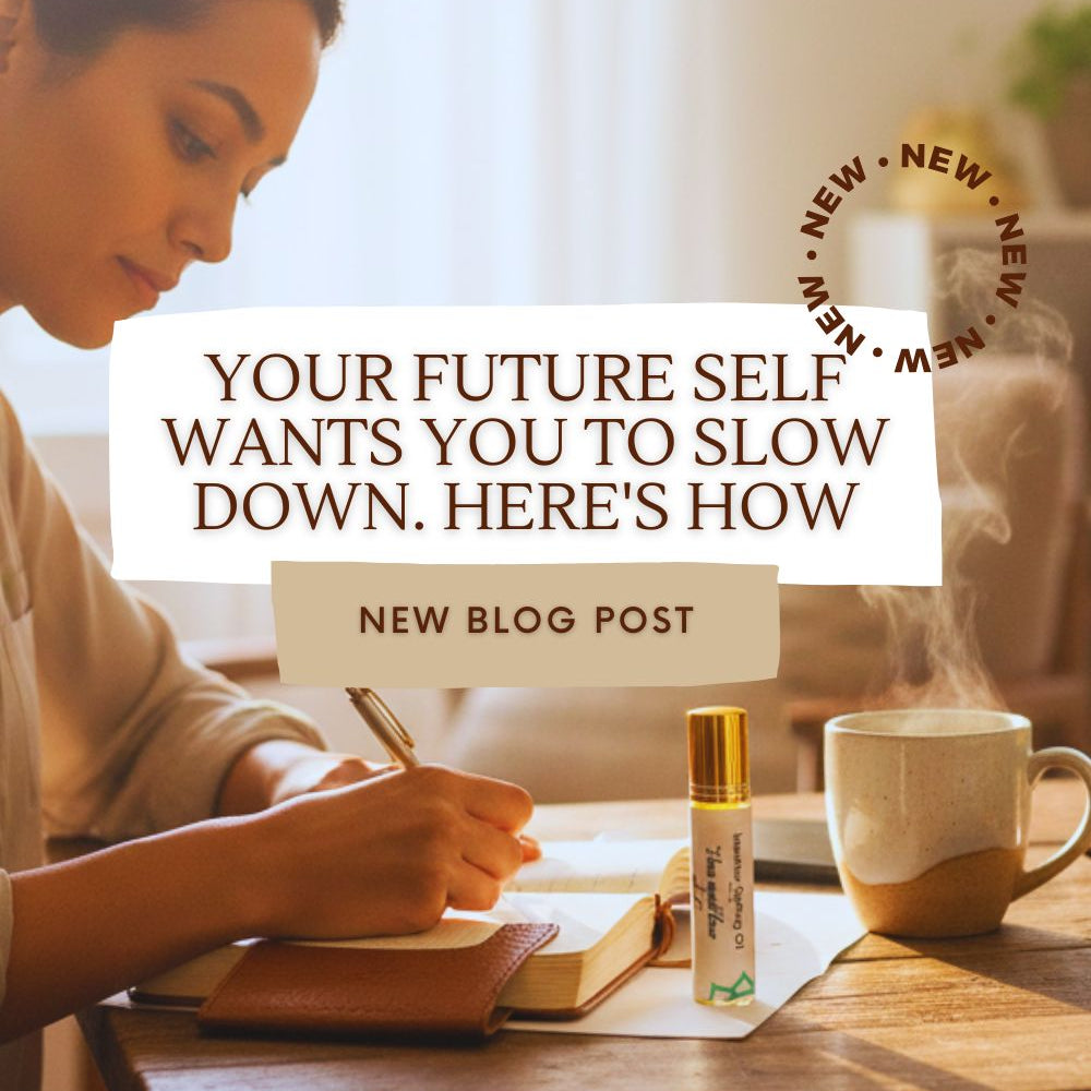 A woman writing in a journal. Next to the journal is an intention setting oil labeled "I love myself flaws and all" and a mug of hot tea