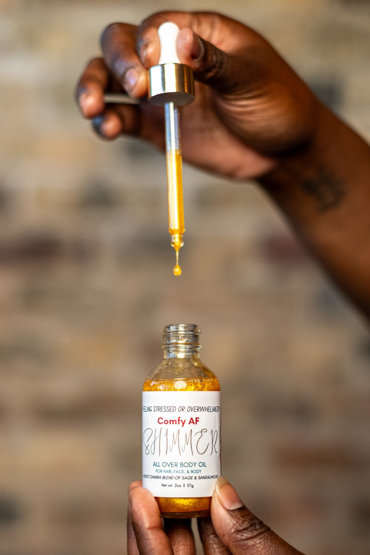 Single drop of shimmering Root Chakra body oil falling from a glass dropper into a jar of Comfy AF natural skincare.
