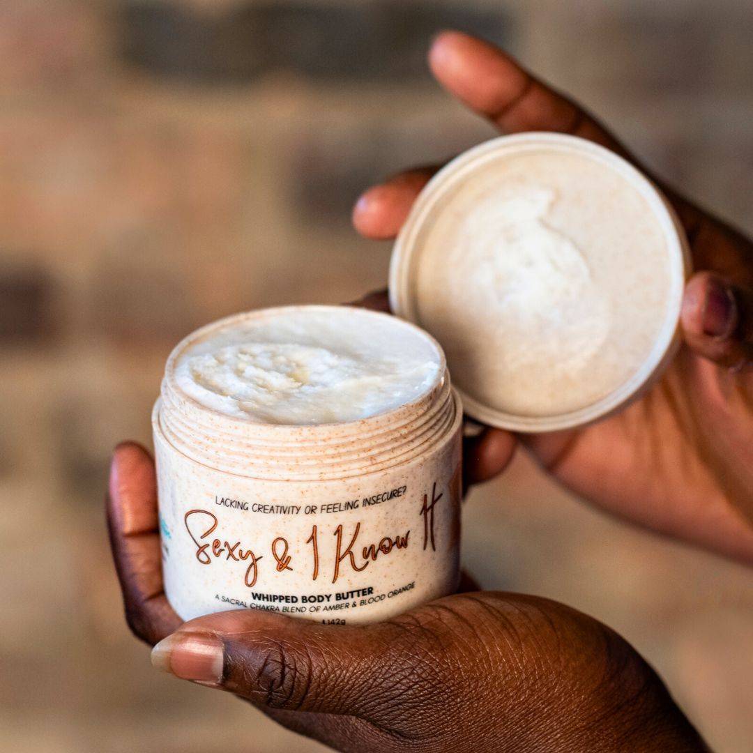 Close up of the creamy texture of Sexy and I Know It Sacral Chakra body butter being held in an African American woman's hands.